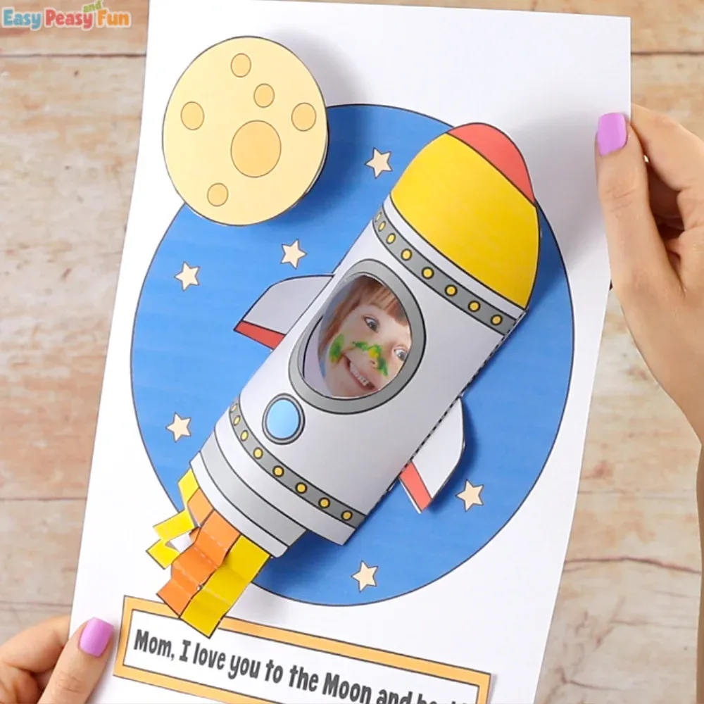 A 3D rocket ship paper craft for Mother's Day with a child's photo in the window, set against a blue moon and stars background.