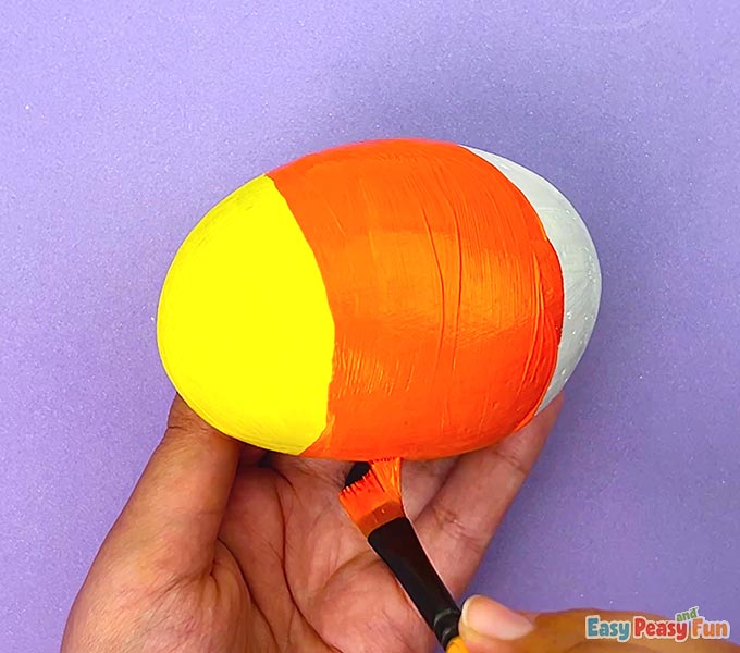 A painted rock showing a yellow head and a bright orange body section.