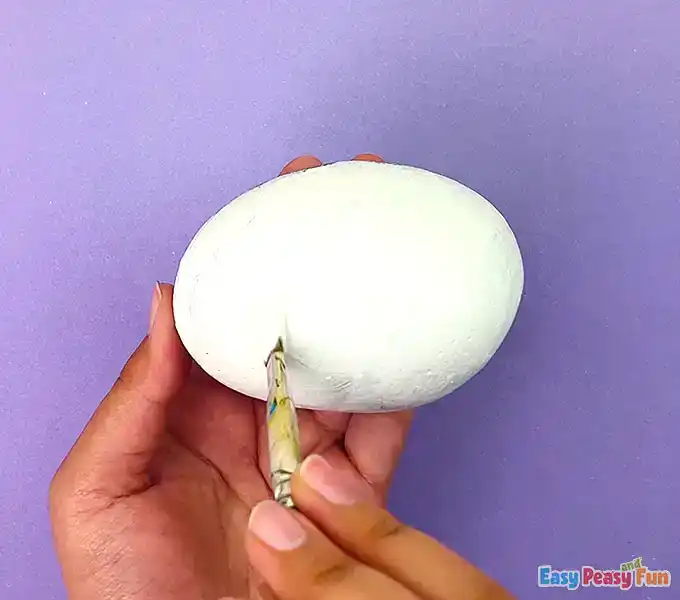 An oval rock being painted with a solid white acrylic base coat.