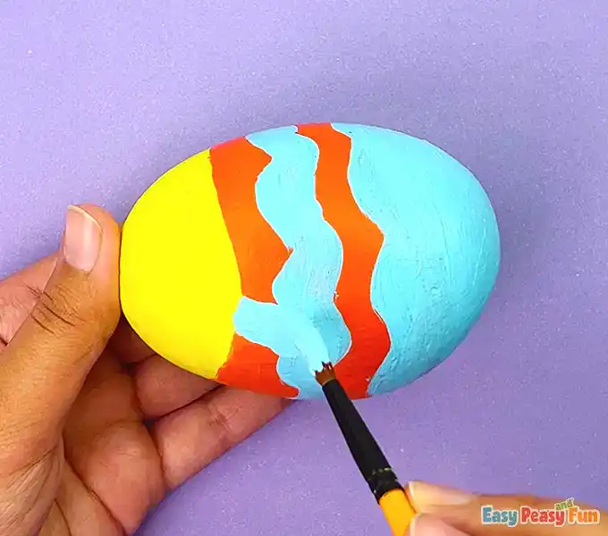 Adding light blue wavy stripes and a small fin to an orange and yellow painted fish rock.