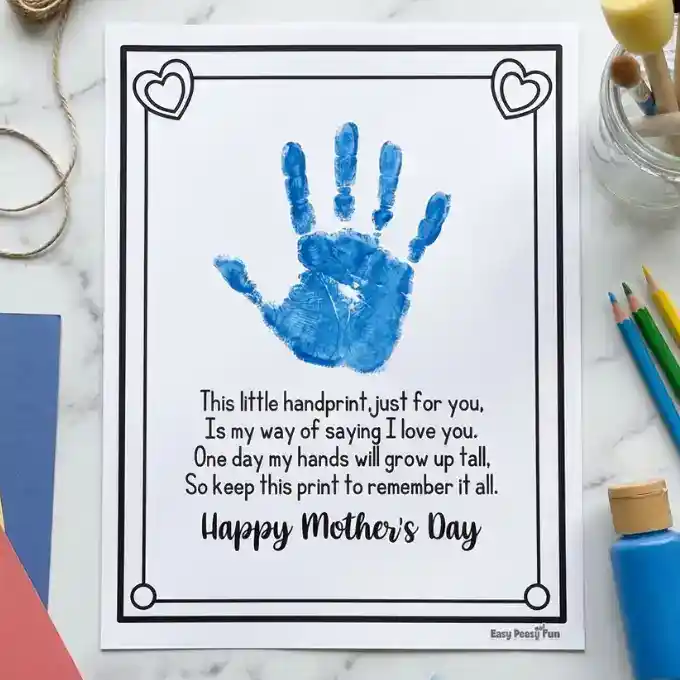 Flatlay of a completed Mother's Day handprint poem printable with blue paint on a marble background, featuring sponge brushes and craft paper.
