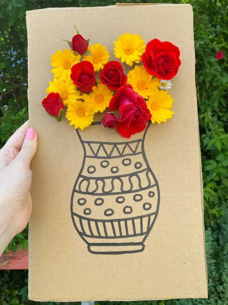 A cardboard flower threading craft featuring a hand-drawn black vase with colorful fresh flowers threaded through the board to create a 3D nature bouquet.