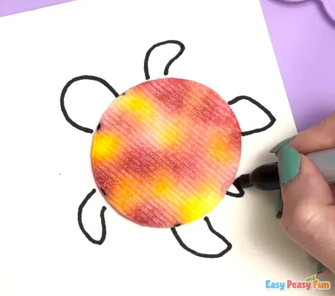 A black marker is used to outline the simple, rounded shapes of the turtle's head, legs, and tail extending from the shell.