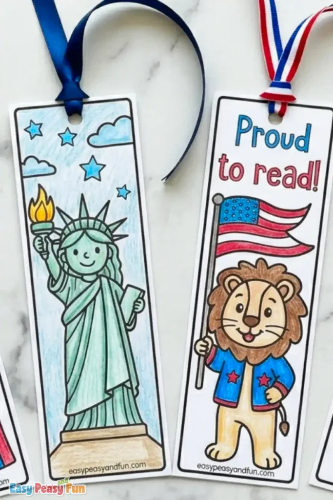 Two hand-colored patriotic bookmarks with ribbons attached, one depicting a cartoon Statue of Liberty and the other a smiling lion holding an American flag below the text "Proud to read!".