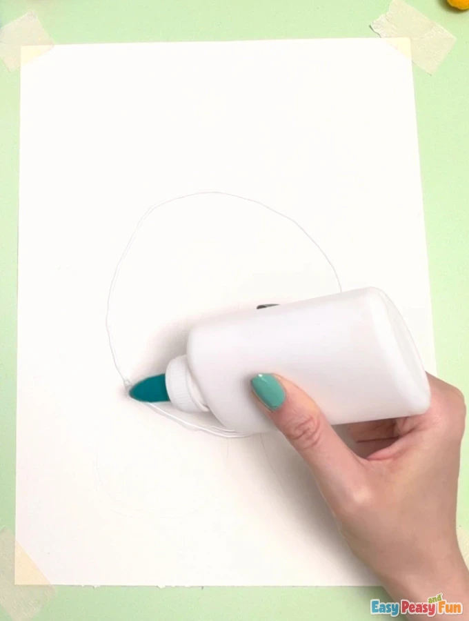 Hand holds a glue bottle, tracing a circular outline onto white paper.