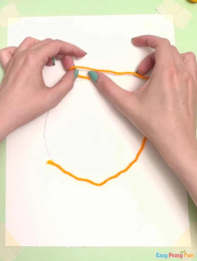 Hands guide orange yarn onto the wet glue circle.
