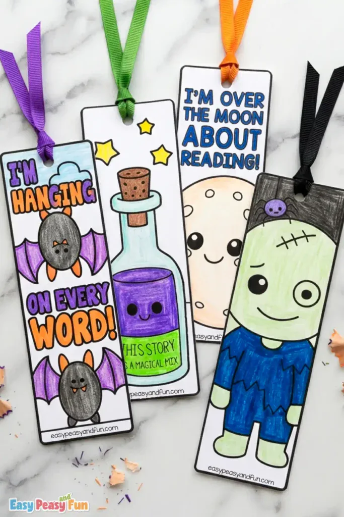 Four colored Halloween bookmarks arranged on a white marble background, featuring bats, a potion bottle, a full moon, and Frankenstein's monster with ribbons.