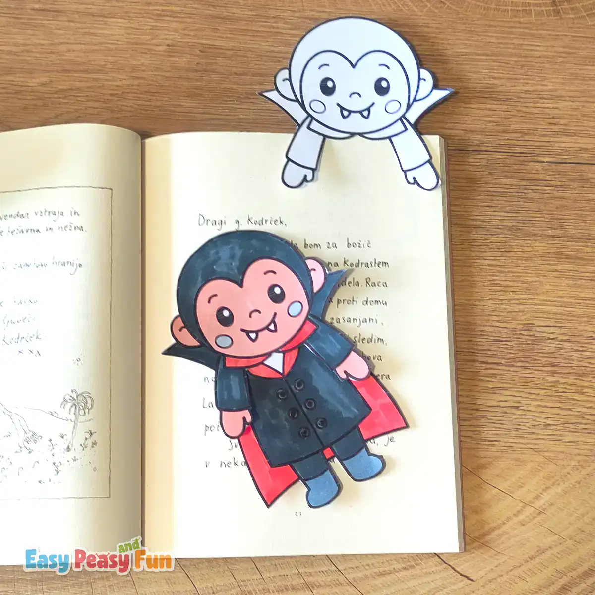 An uncolored vampire template gripping a book page, with a colored vampire bookmark below.