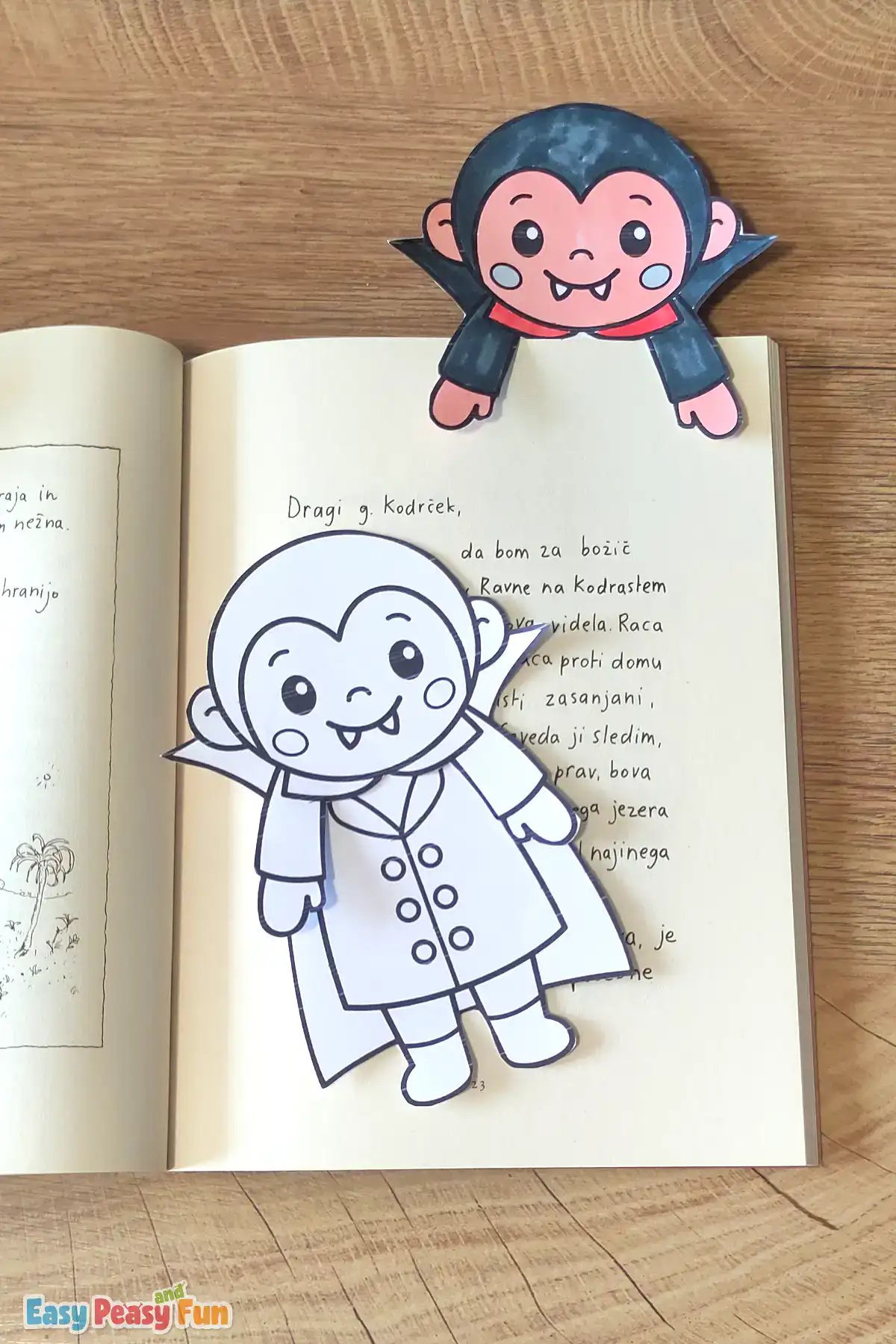A colored vampire bookmark at the top of an open book, with an uncolored vampire on the page below.
