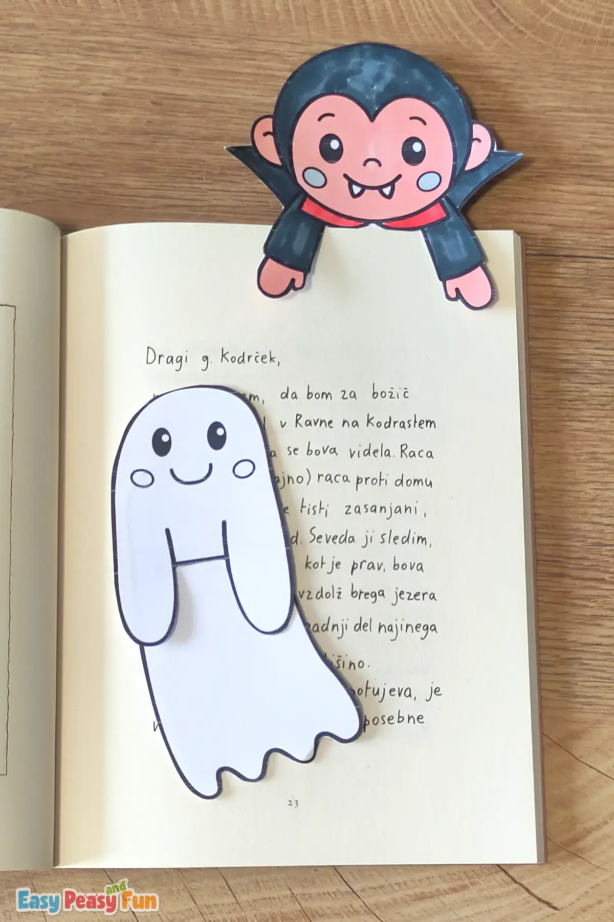 A colored vampire bookmark at the top of an open book, with an uncolored ghost resting on the page below.