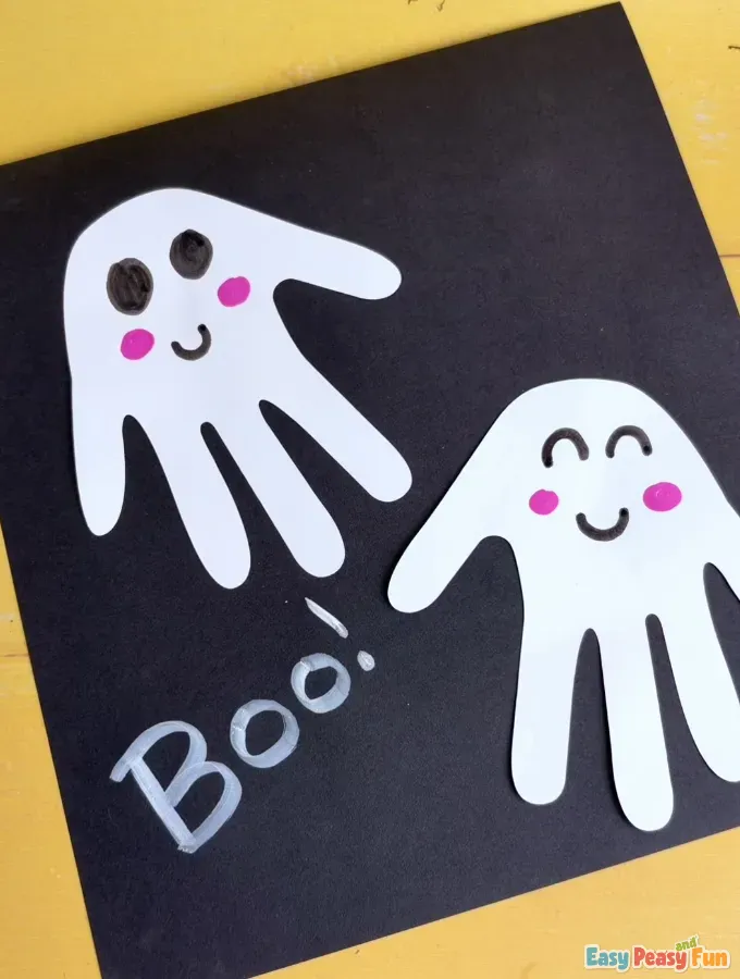 The finished Halloween ghost handprint art on black paper featuring two smiling ghosts and white "Boo!" text.