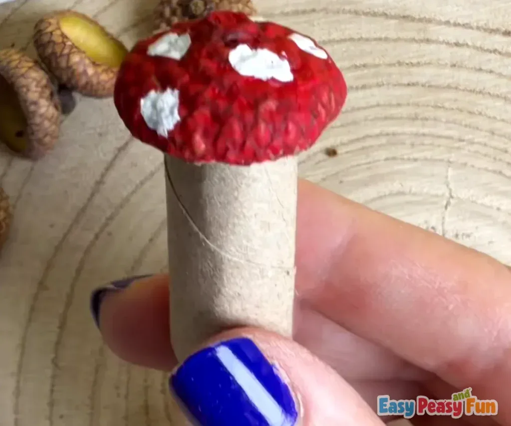 The completed handmade acorn mushroom sits upright, showing off its red cap and white polka dots.