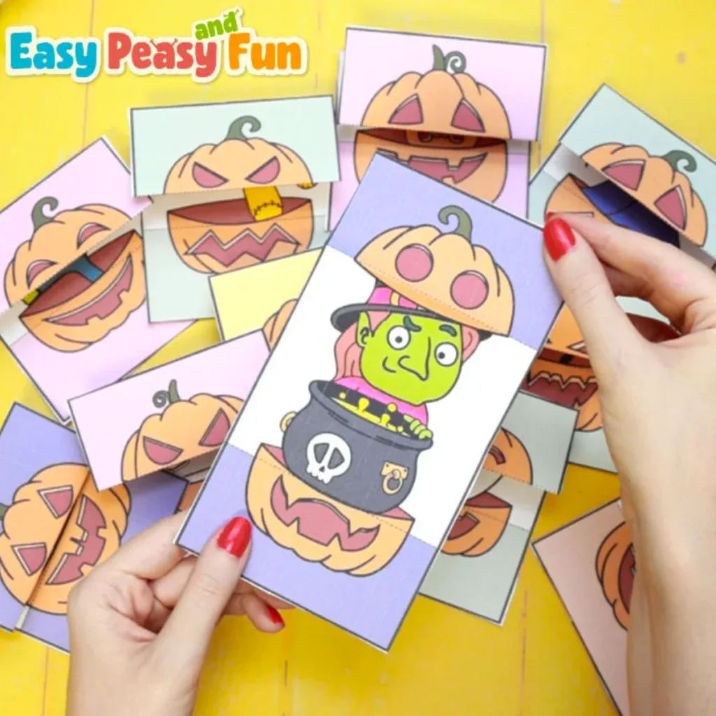 Hands holding a paper Halloween surprise card open to reveal a green witch inside a cauldron, surrounded by several other similar cards on a yellow surface.