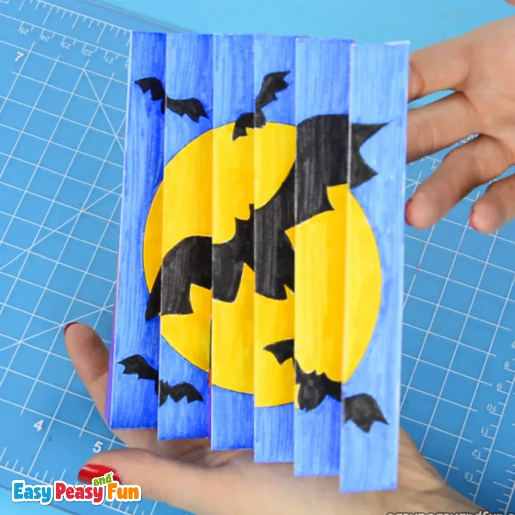 A person holding a folded Halloween agamograph art piece featuring flying bats.