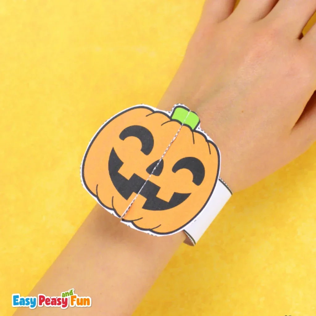 A person wearing a papercraft pumpkin bracelet on their wrist.