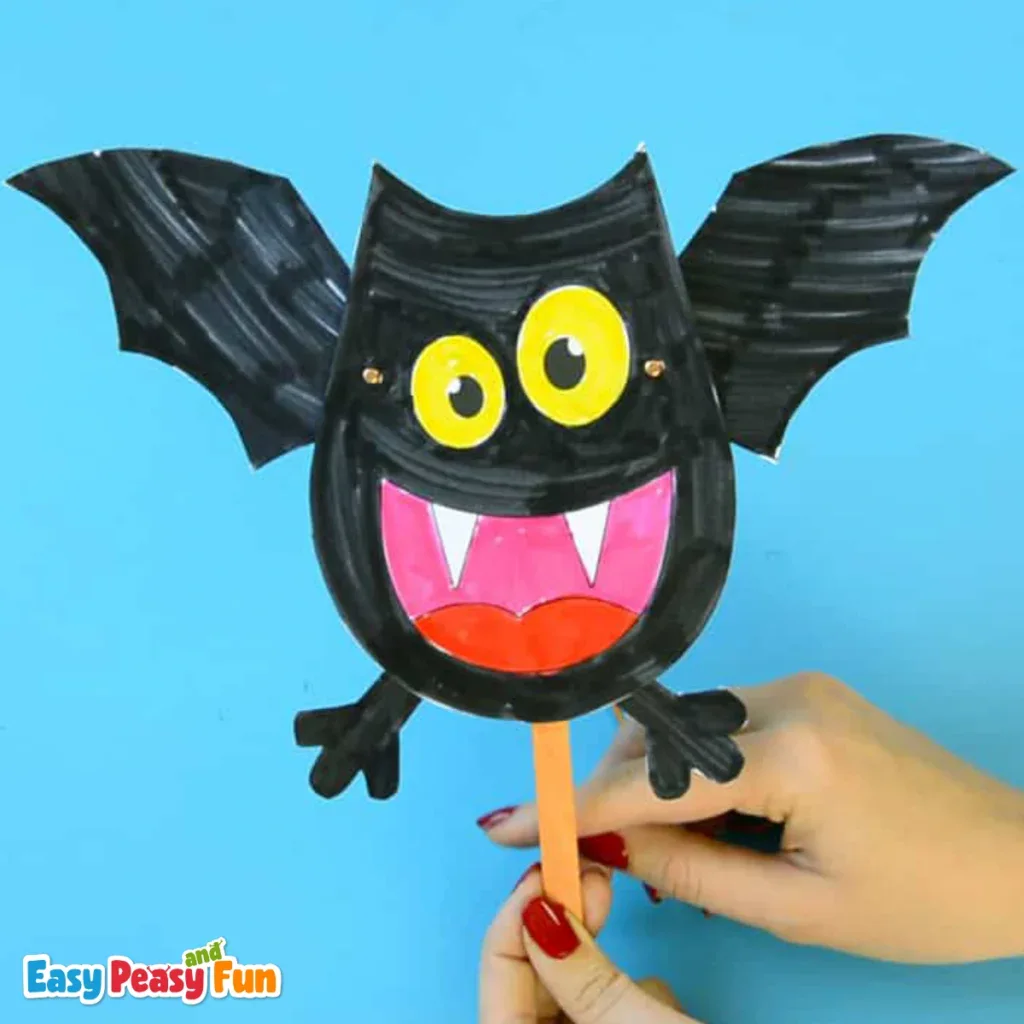 A person holding a movable black paper bat puppet on a popsicle stick.