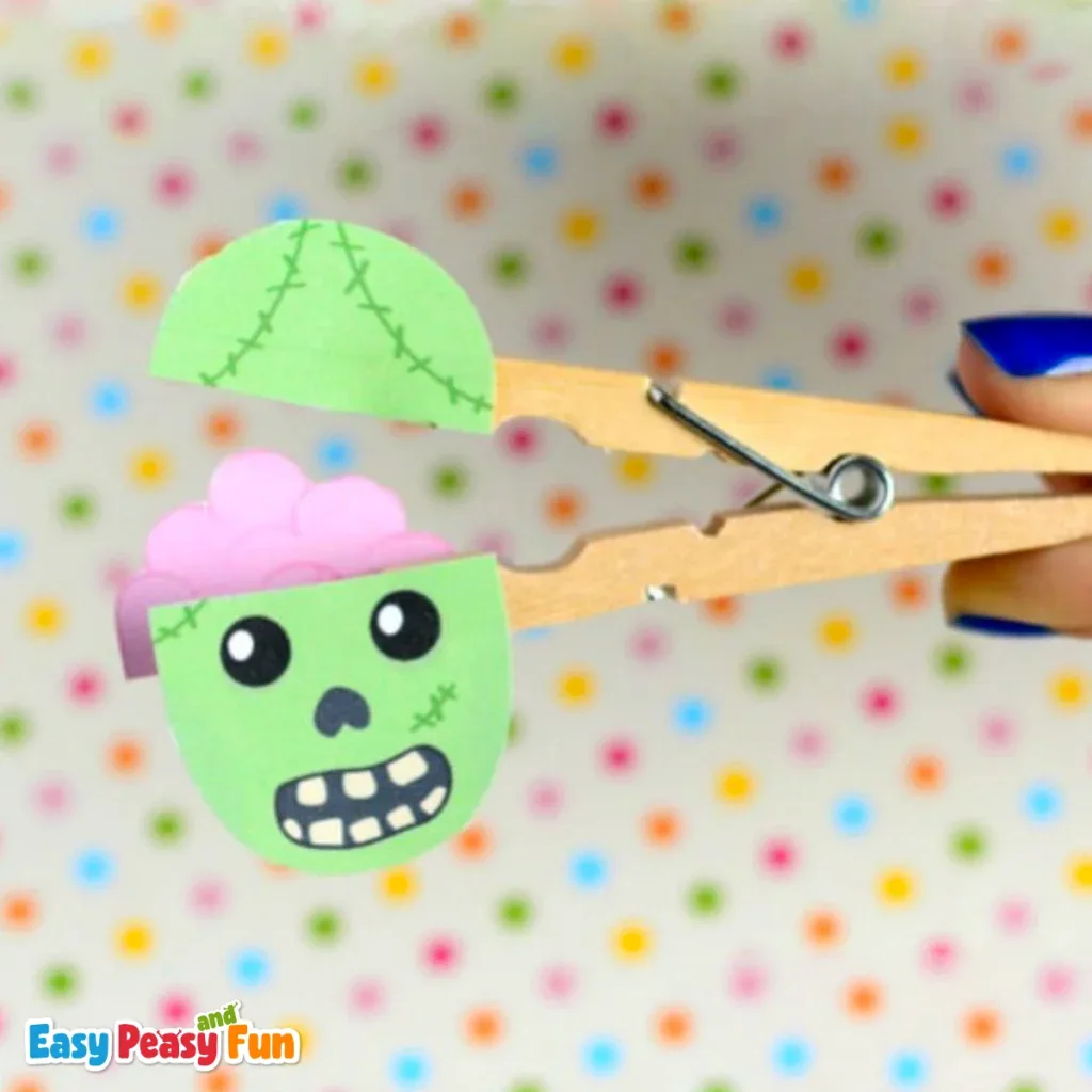 A person pinching a handmade zombie clothespin puppet that opens its mouth to reveal a pink brain,.