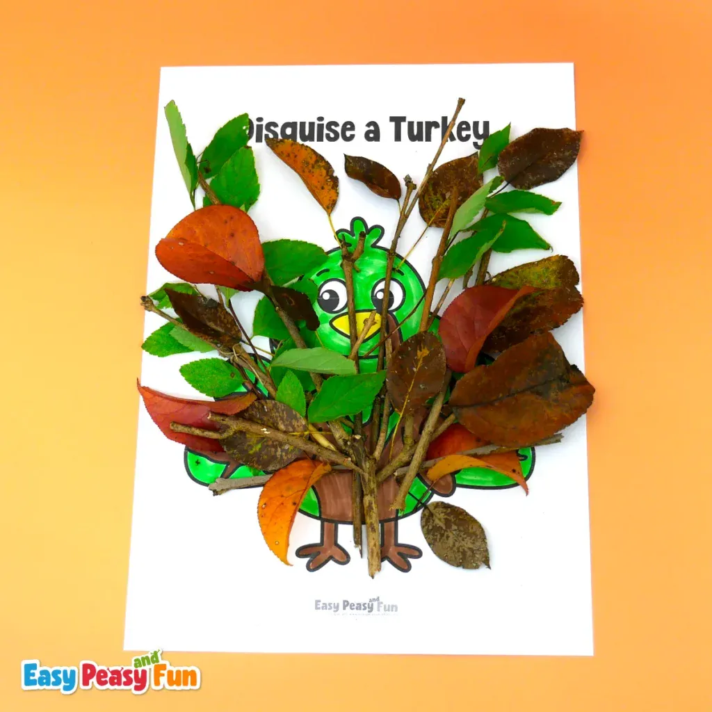 A paper turkey craft disguised as a tree, hidden behind real twigs, green leaves, and brown autumn leaves.