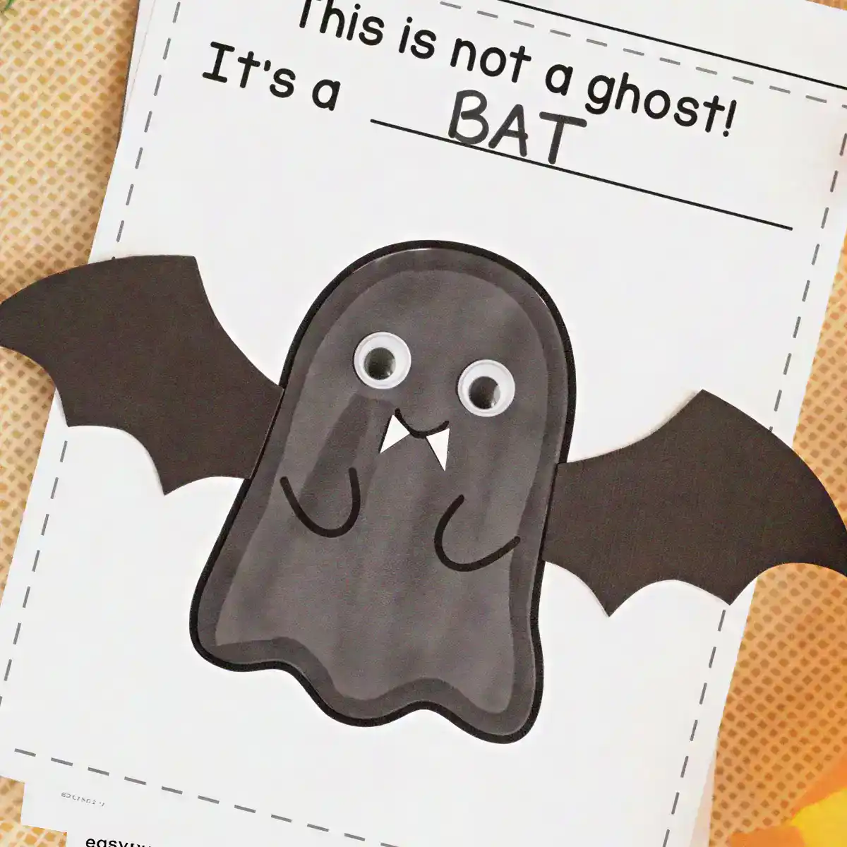 Dark gray ghost craft with googly eyes, white fangs, and black paper wings made to look like a bat.